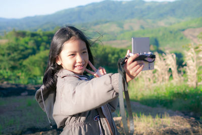 Smiling girl taking selfie with camera while standing against landscape