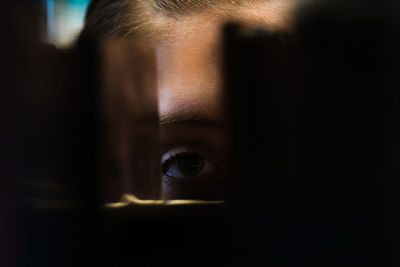 Close-up portrait of teenage girl peeking through bookshelf