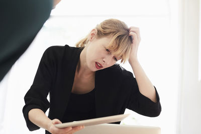 Confused businesswoman scratching head while using digital tablet in office