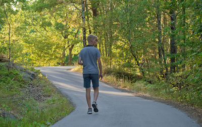 Rear view of man walking on road along trees