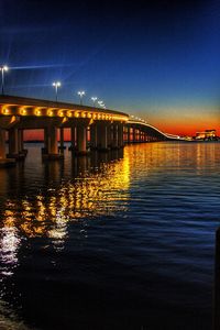 Illuminated bridge over river against sky at night