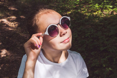 Girl wearing sunglasses while standing by tree trunk in forest