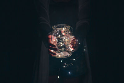 Midsection of person holding string lights in jar