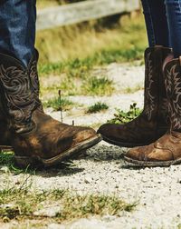 Low section of friends wearing cowboys boots on field