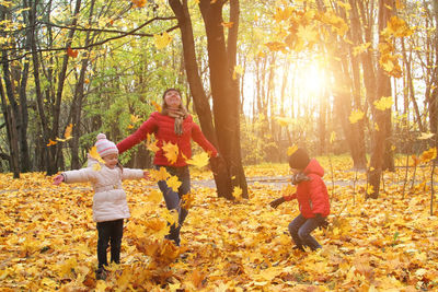 Smiling mother with kids playing in forest during autumn