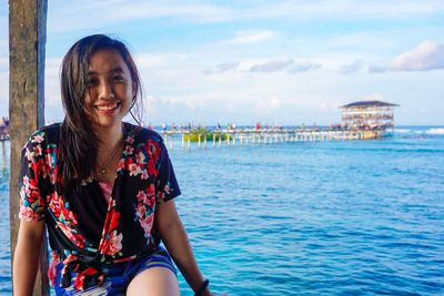 Portrait of smiling woman sitting on sea against sky