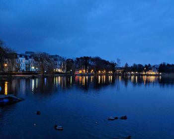 Scenic view of river against illuminated buildings at dusk