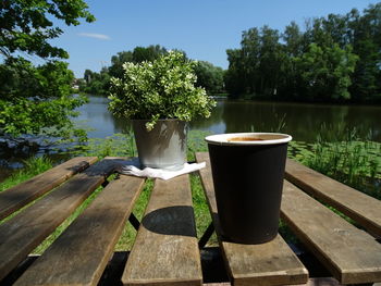 Tea cup on table by lake against trees