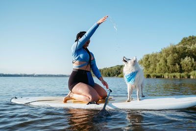 Woman with locs playing with her pet japanese spitz while sitting on the sup board on the lake
