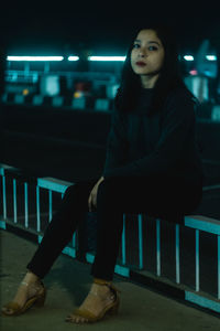 Portrait of young woman sitting on illuminated floor at night