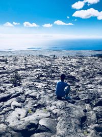 Rear view of man sitting on beach against sky