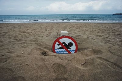 Warning sign on beach against sky