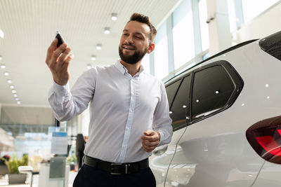 Smiling car dealer holding key at showroom