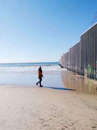 Rear view of man walking on beach against clear sky