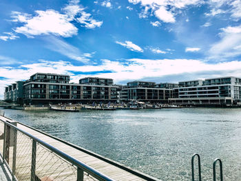 Buildings by river against sky in city