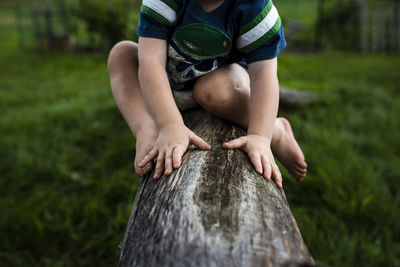 Low section of boy sitting on log in backyard