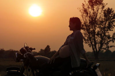 Pregnant woman sitting on motorcycle against clear sky during sunset