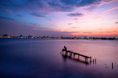 Man sitting on broken pier in sea during sunset