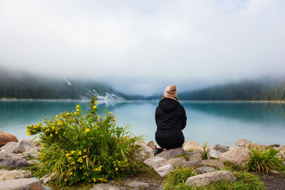 Man sitting on rock by lake against sky