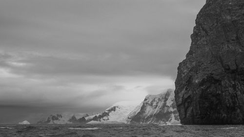 Black and white photo of sea against snowcapped mountain 