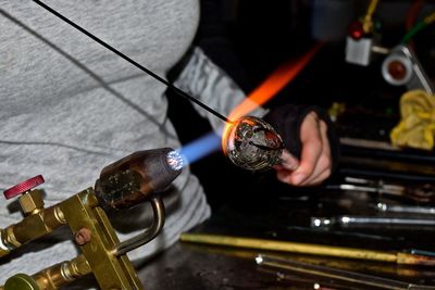 Midsection of young woman making glass with flaming torch in factory