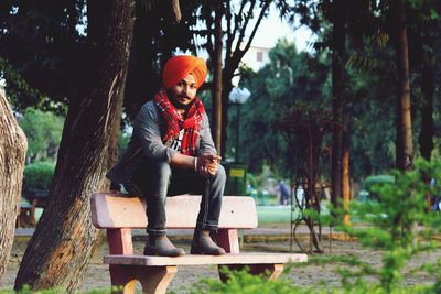 Portrait of smiling man sitting on seat against trees