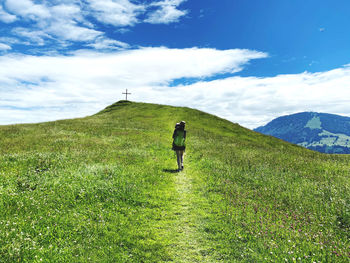 Rear view of woman walking up a grassy hill against mountains carrying child and backpack
