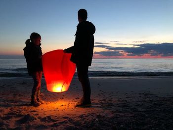 Silhouette men standing on beach against sky during sunset