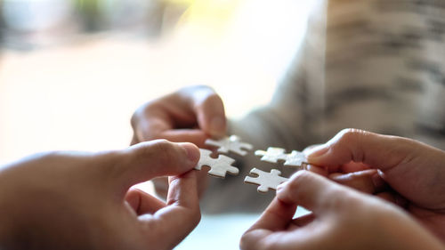 Midsection of people attaching jigsaw puzzle at home