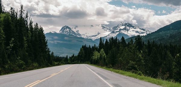 Road amidst trees and mountains against sky