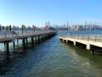 Pier over river by city against clear sky