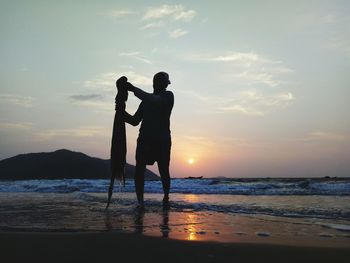 Fisherman holding net while standing against sea during sunset