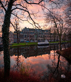 Reflection of bare trees in lake against sky during sunset