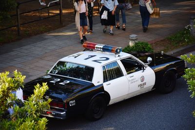 Low section of people walking by police car on street