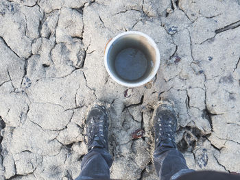 Low section of man standing by empty bucket on cracked landscape