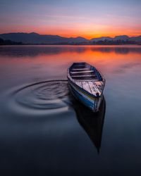 Boat moored on lake against sky during sunset