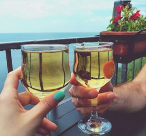 Cropped hands of couple toasting alcohol glasses by sea