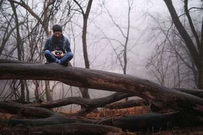 Man sitting on fallen tree in forest
