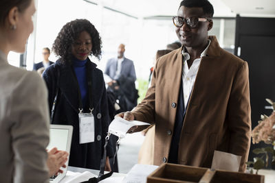 Businessman holding id card while talking to receptionist at registration counter