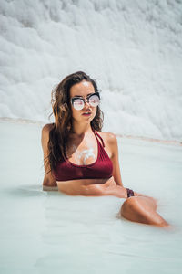 Young woman wearing bikini while sitting in sea