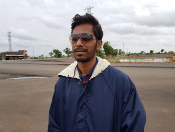 Young man wearing sunglasses standing on road against cloudy sky