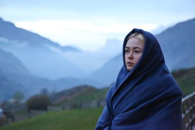 Beautiful woman wrapped in blanket standing on mountain against sky