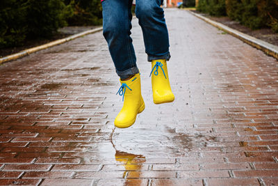 Jumping in puddle. female legs in yellow rubber boots jumping on the puddle. carefree young woman