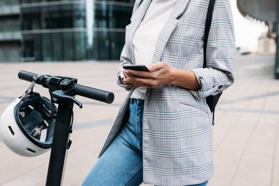 Cropped shot of female in casuals using an app on a cell phone for unlocking electric push scooter	