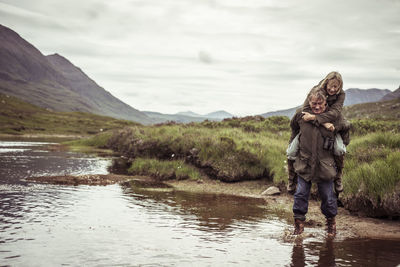Retired couple piggy back carry across remote mountain fishing river