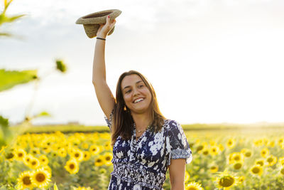 Smiling young woman with yellow flowers on field against sky