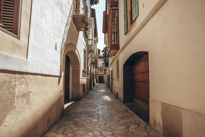 Empty alley amidst old buildings against sky during sunny day