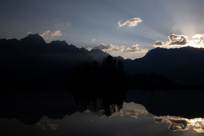 Scenic view of lake and silhouette mountains against sky at sunset