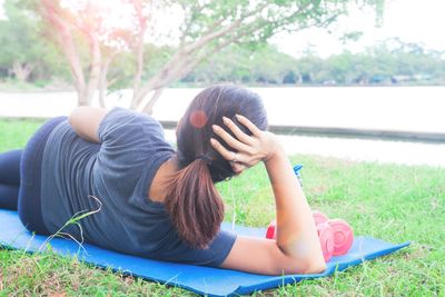 Rear view of woman lying on exercise mat at park