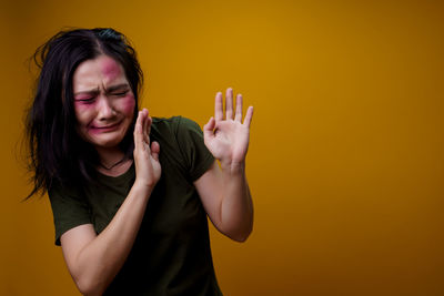 Portrait of beautiful young woman standing against yellow background